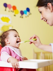 mom giving homogenized food to her daughter on high chair. Vertical shape